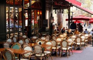 Where to Eat Near the Eiffel Tower (Local Favorite Spots + Map) Paris café terrace with classic bistro chairs and red awnings, people dining outdoors on a sunny day.