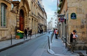 Le Marais Neighborhood Guide Narrow cobblestone street in Le Marais, Paris, with people walking and old stone buildings