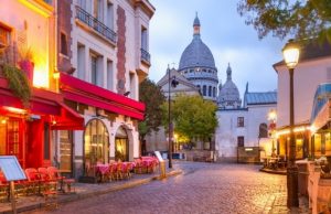 Paris at Night: Best Evening Walks & Illuminations (Map + Safety Tips) Montmartre’s cobblestone street and Sacré-Cœur at blue hour with café lights in Paris