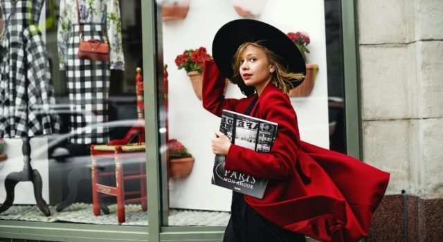 Woman in a red coat and black hat walking past a Paris boutique — stylish spring outfit