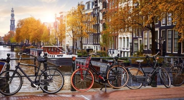 Bicycles along an Amsterdam canal at sunrise with historic Dutch houses in the background