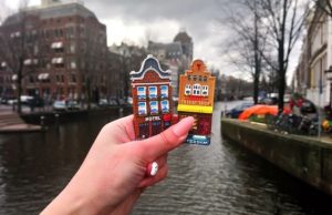 Amsterdam 3-Day Itinerary: The Perfect Balance of Iconic Sights & Local Life Hand holding Amsterdam souvenirs in front of a canal — iconic Dutch houses and waterway in the background.
