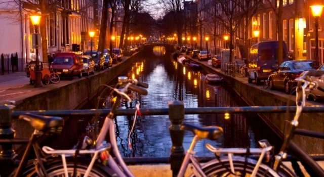 amsterdam-non-touristy-things-to-do-canal-evening Evening canal view in Amsterdam with warm street lights and bicycles on a bridge