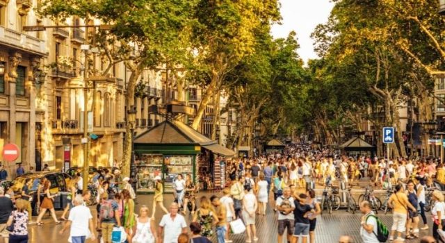 Crowds on La Rambla in Barcelona at golden hour, street kiosks and trees lining the boulevard