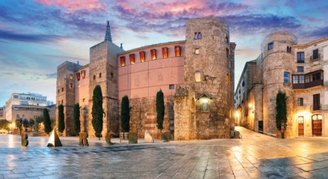barcelona-gothic-quarter-placa-nova-barcino-cover Roman walls and the “Barcino” sculpture at Plaça Nova in Barcelona’s Gothic Quarter at sunset.