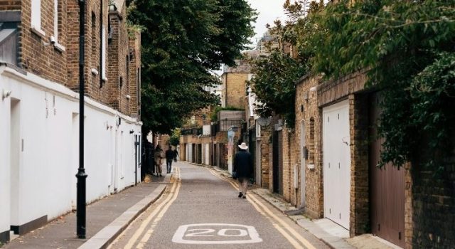 Narrow residential street in London with brick houses and people walking, showcasing the city's quiet local neighborhoods