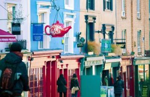 London Neighborhood Guide: Where to Stay for Every Travel Style Colorful street scene in Notting Hill with boutique shops, signs, and people walking along Portobello Road