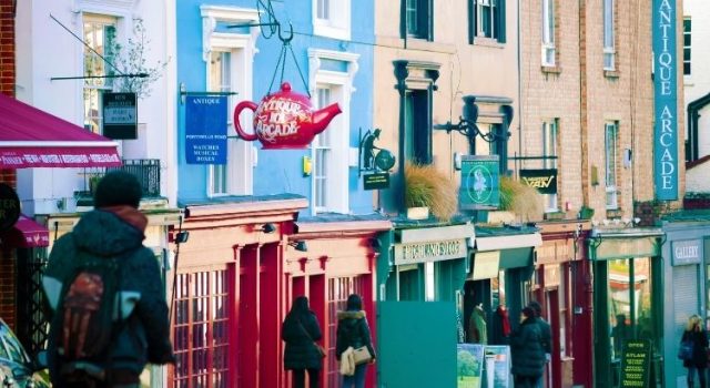 Colorful street scene in Notting Hill with boutique shops, signs, and people walking along Portobello Road