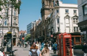 London in Summer: What to Wear (Packing List + Outfit Ideas) Crowded sunny street in London with red phone booths and people wearing summer outfits.