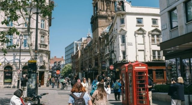 london-summer-street-style Crowded sunny street in London with red phone booths and people wearing summer outfits.