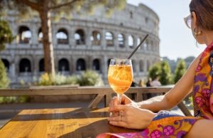Rome’s Aperitivo Guide: Top Bars for Spritz & Small Bites Woman enjoying an Aperol spritz with a view of the Colosseum in Rome during aperitivo hour