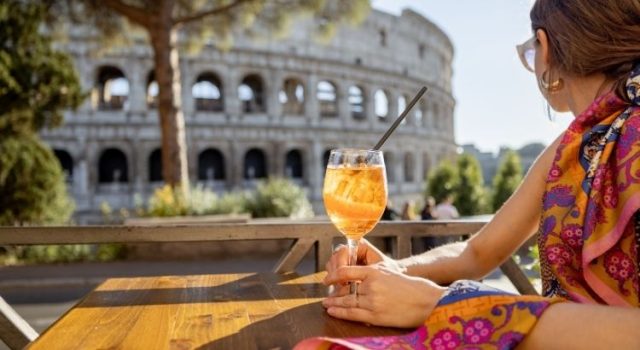 rome-aperitivo-spritz-colosseum-hero Woman enjoying an Aperol spritz with a view of the Colosseum in Rome during aperitivo hour
