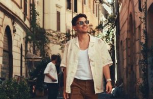 What to Wear in Rome by Season (Packing List + Dress Codes) Traveler in a light linen shirt and sunglasses walking a leafy Roman side street