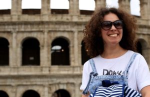 Rome in Summer: What to Wear (Packing List + Outfit Ideas) Woman in a T-shirt and denim overalls with sunglasses in front of the Colosseum in Rome