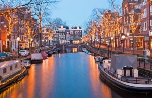Amsterdam Essentials: First-Time Visitor Guide (Transportation, Money, Safety & Local Tips) Amsterdam canal at dusk with illuminated trees, boats, and traditional Dutch houses—iconic cityscape for first-time visitors.