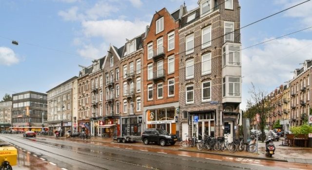Street view of Amsterdam with traditional narrow buildings, bikes and tram line — local neighborhood scene