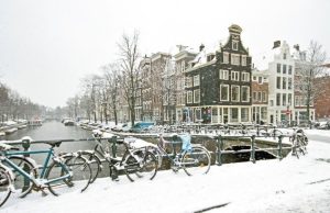 Amsterdam in Winter: Christmas Markets, Light Festival & Cozy Things to Do Snow-covered bicycles and canal houses in Amsterdam during winter on a snowy day