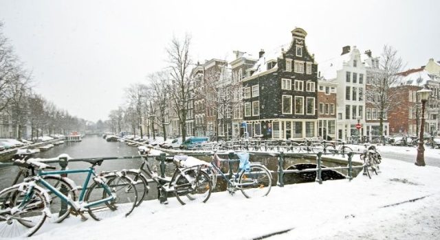 Snow-covered bicycles and canal houses in Amsterdam during winter on a snowy day
