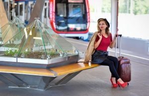 Rome Metro Tickets & Prices 2025: Is the Day Pass Worth It? Young woman sitting on a bench at a metro station with a suitcase beside her, wearing red heels and a red top, modern train visible in the background.