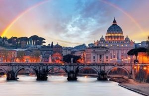 Getting to the Vatican by Metro: Ottaviano or Cipro? Scenic view of Rome at sunset with the Tiber River, an illuminated historic bridge, St. Peter’s Basilica in the background, and a rainbow arching across the sky.