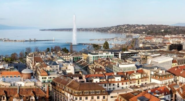 geneva-lake-jet-deau-old-town-view-2026 Panoramic view of Geneva Old Town and Lake Geneva with the Jet d’Eau fountain, a classic backdrop for fondue spots like Bains des Pâquis.
