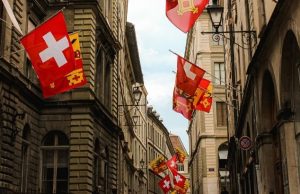 Weekend in Geneva: 2-Day Itinerary for Science & Chocolate Lovers (2026) Swiss and Geneva flags lining a historic street in Geneva Old Town, part of a weekend itinerary for culture, science, and chocolate lovers.