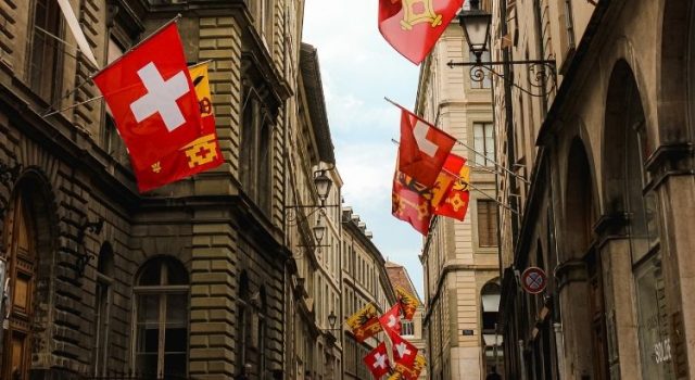 Swiss and Geneva flags lining a historic street in Geneva Old Town, part of a weekend itinerary for culture, science, and chocolate lovers.
