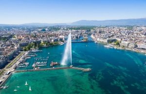 Geneva in Summer: Where to Swim? Bains des Pâquis vs. The Rhône (2026) Aerial view of Lake Geneva and the Jet d’Eau in summer, highlighting popular swimming areas near Bains des Pâquis and the Rhône.