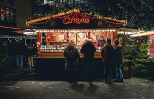 Geneva in Winter: L’Escalade Festival, Chocolate Pots & Christmas Markets (2026) People ordering crêpes at a cozy outdoor market stall in Geneva during winter, with festive lights and a warm atmosphere.