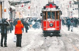 Istanbul in Winter Diaries: Melancholy, Fog & Boza (2026) Historic red tram on Istiklal Street during snowfall in Istanbul with pedestrians and winter atmosphere